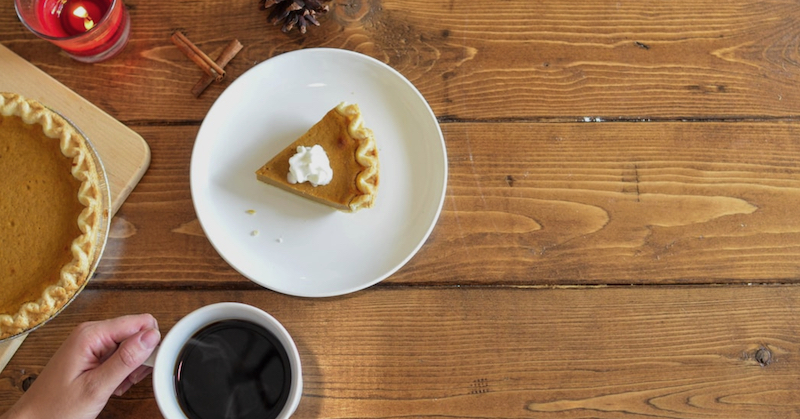 Slice of pumpkin pie with whipped cream and a cup of coffee on a rustic wooden table.