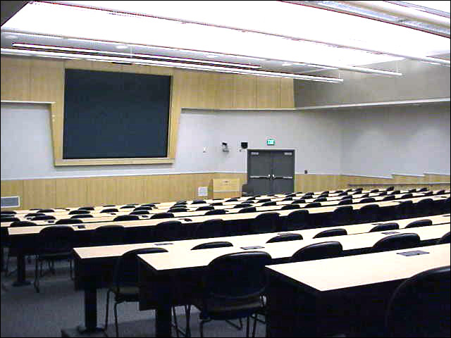 A large lecture hall seating 140 with a view of a podium and a large screen.