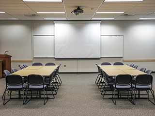 A large classroom seating 60 with a screen, whiteboard, and lecturn. The seating is organized for group discussion.