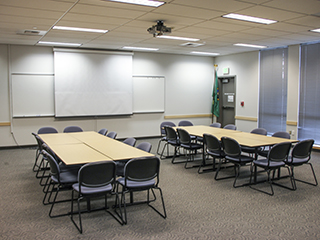 A large classroom seating 60 with a screen, whiteboard, and lecturn. The seating is organized for group discussion.