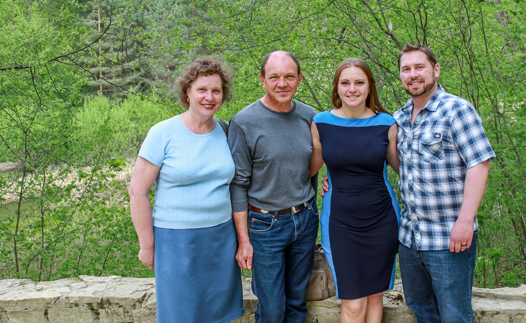 Kathryn and her family smiling to the camera, outside, with lush green trees behind them